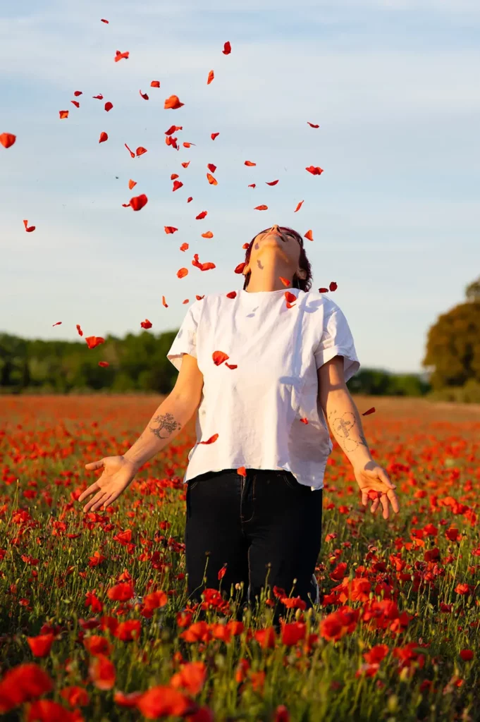 femme tête en arrière dans un champ de coquelicots et sous une pluie de pétales de coquelicots